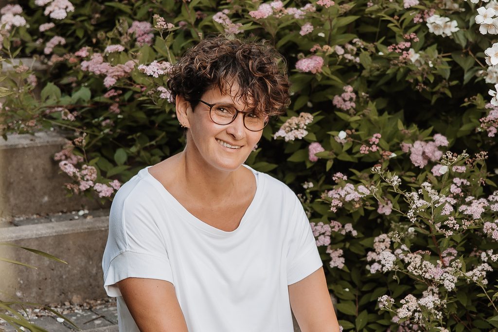 Doris Fredl im Garten vor blühenden Sträuchern.